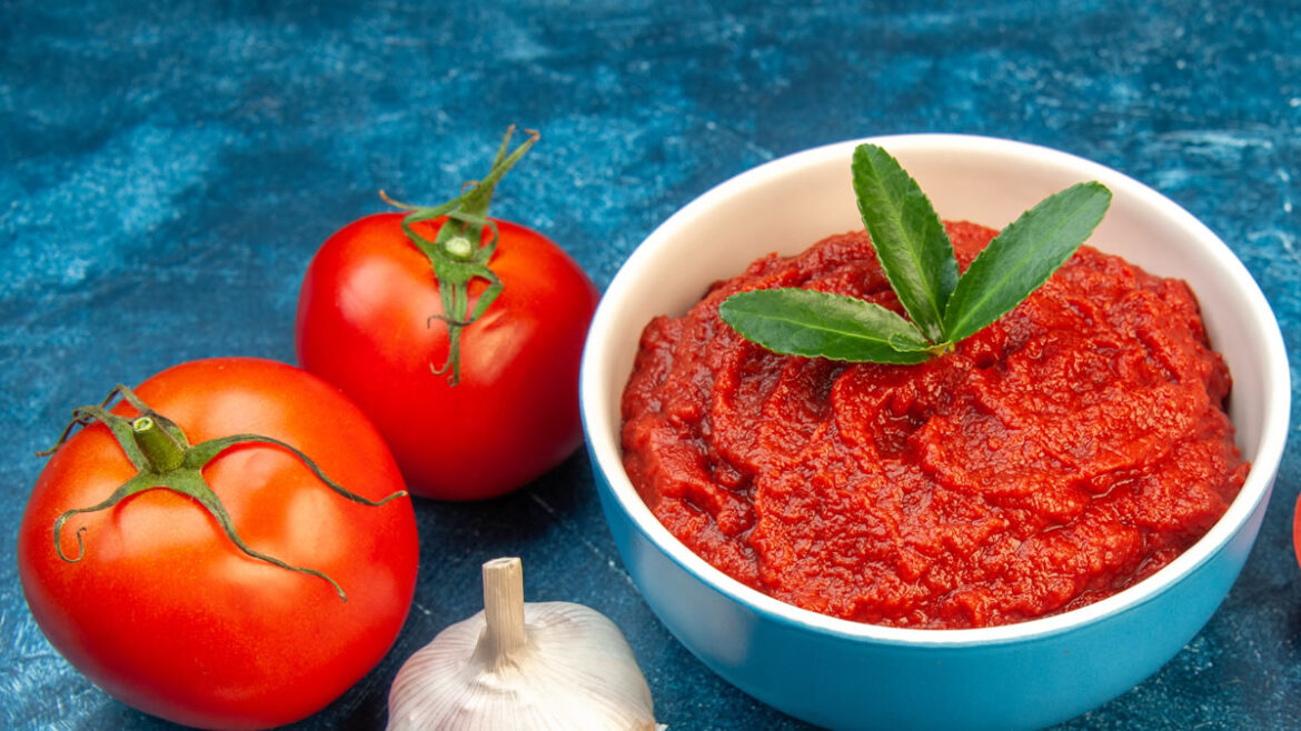 Tomatenmark in Schale mit frischen Tomaten und Knoblauch auf blauem Untergrund – Symbolbild für gesunde Ernährung und Lycopin.