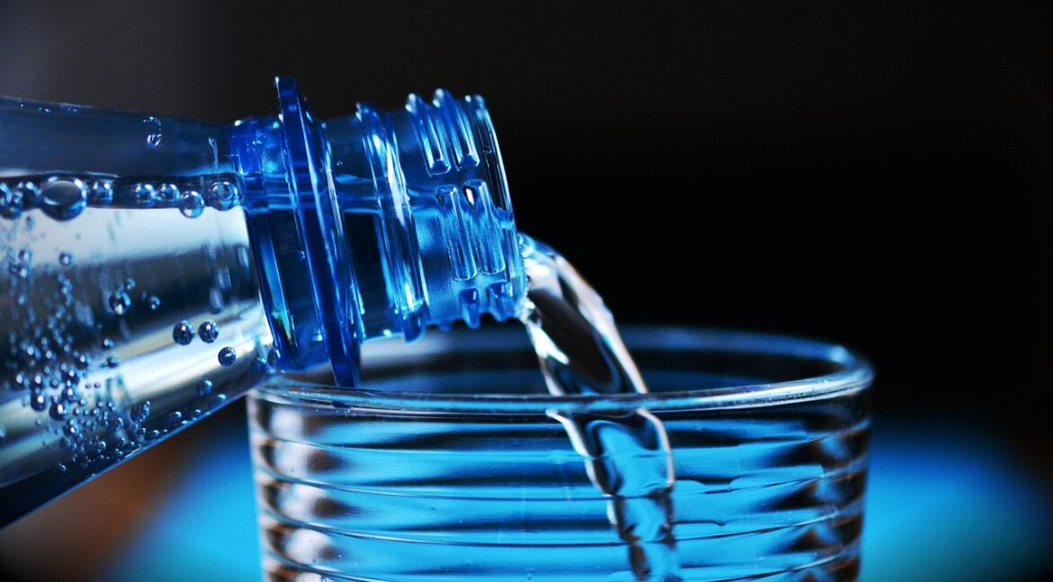 Mineralwasser wird aus einer blauen Kunststoffflasche in ein Glas gegossen