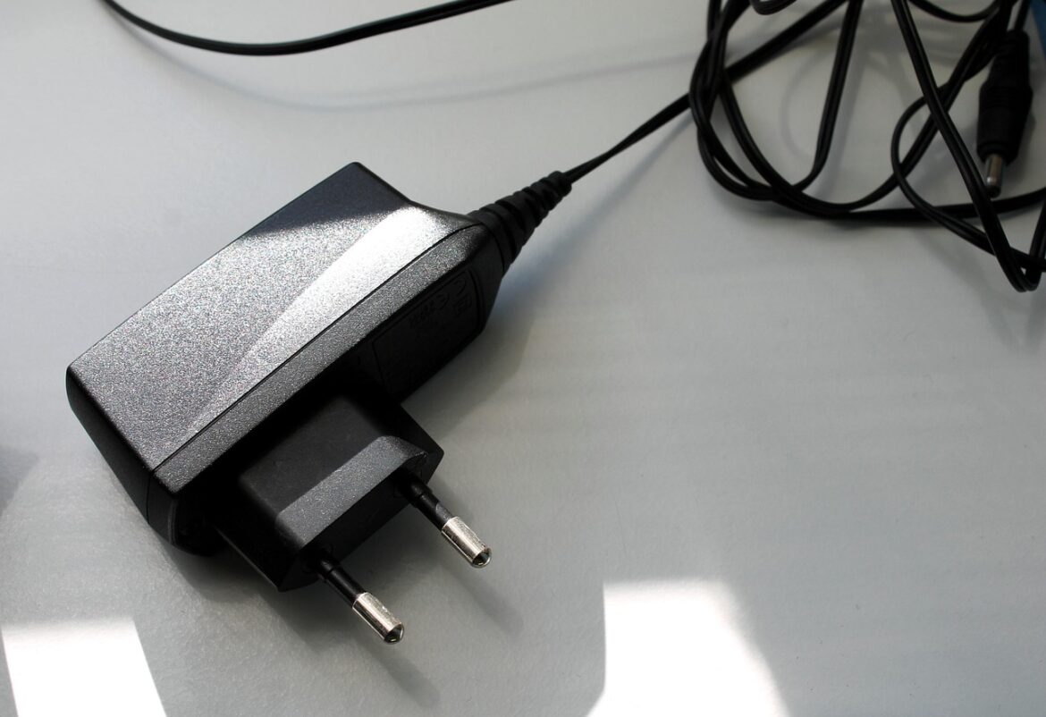 Schwarzes Steckernetzteil mit Kabel auf einem hellen Tisch, beleuchtet durch Sonnenlicht.